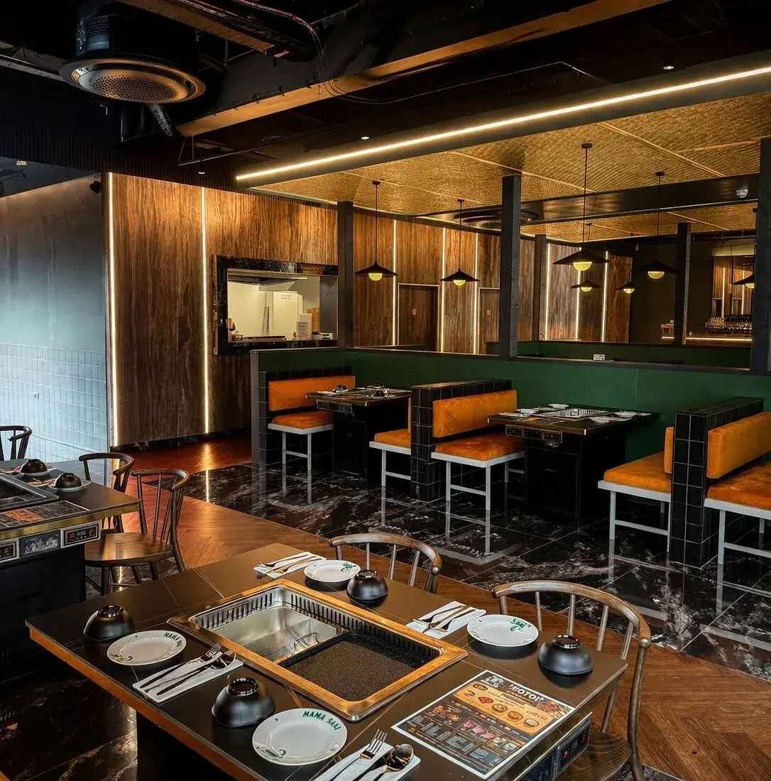 Rows of caramel velvet booths against bottle green panelling, each table set with a hotpot and griddle