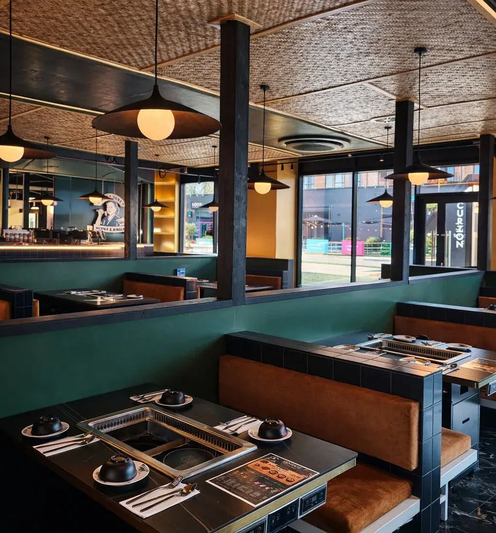 Booths under the woven rattan ceiling, with pendant lights and windows looking out onto The Riverside
