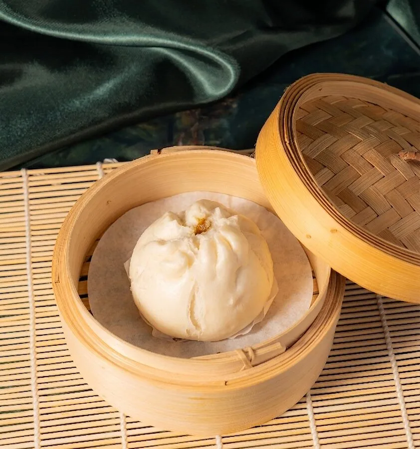 A soft steamed chicken bun in an open bamboo basket