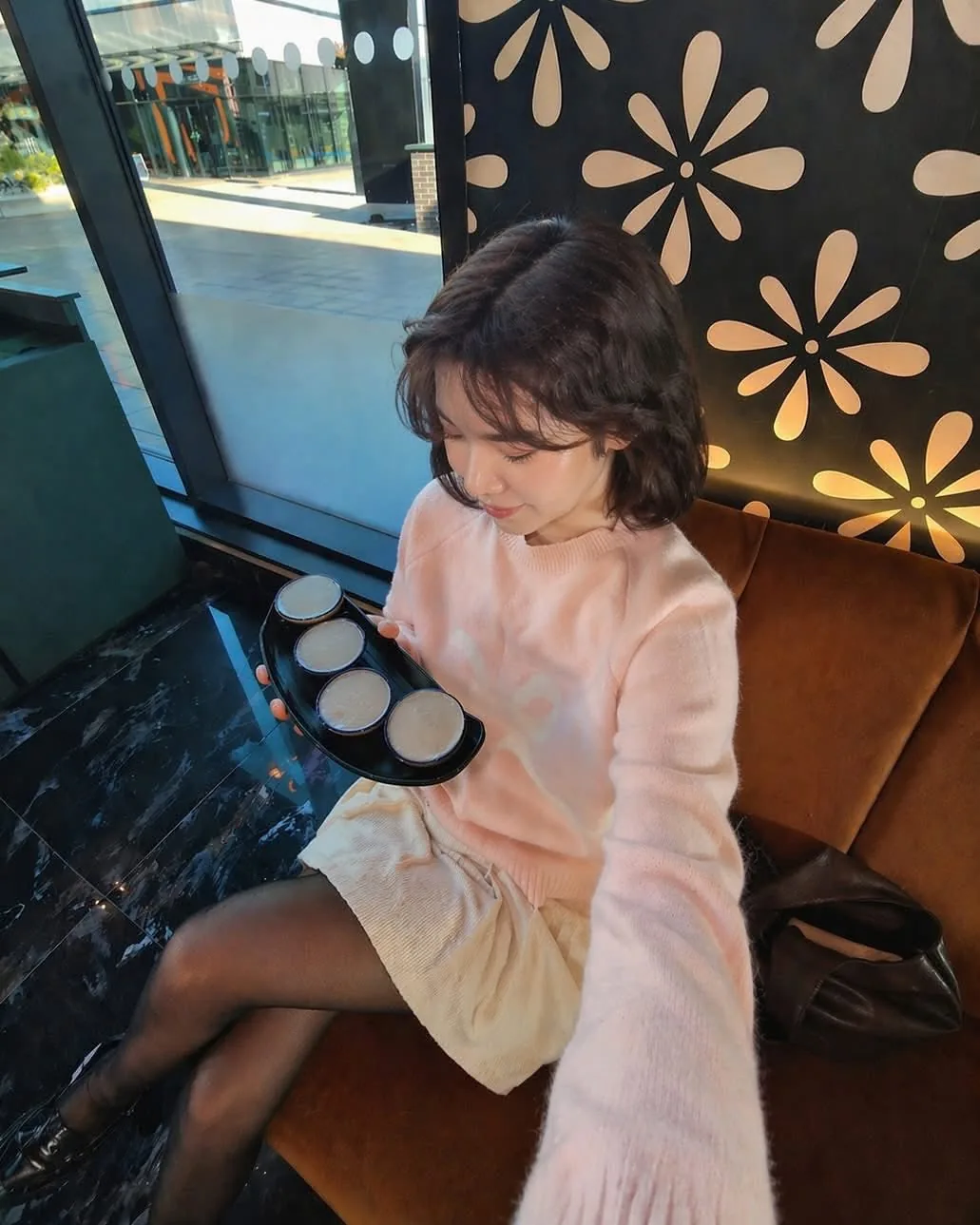 A guest on a velvet banquette holding a tray of four desserts by the window