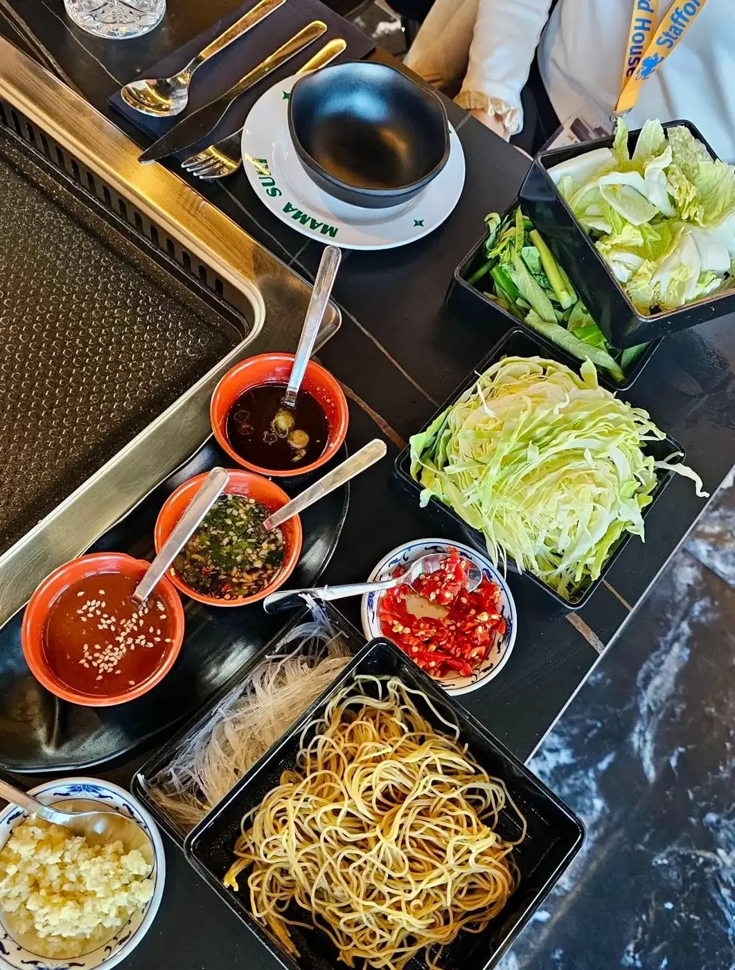 Bowls of dipping sauces, fresh chilli and garlic beside noodles and greens at a Mama Suki table